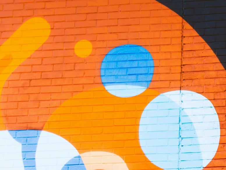 Orange and blue graffiti on a brick wall, taken from a photo by Humphrey Muleba